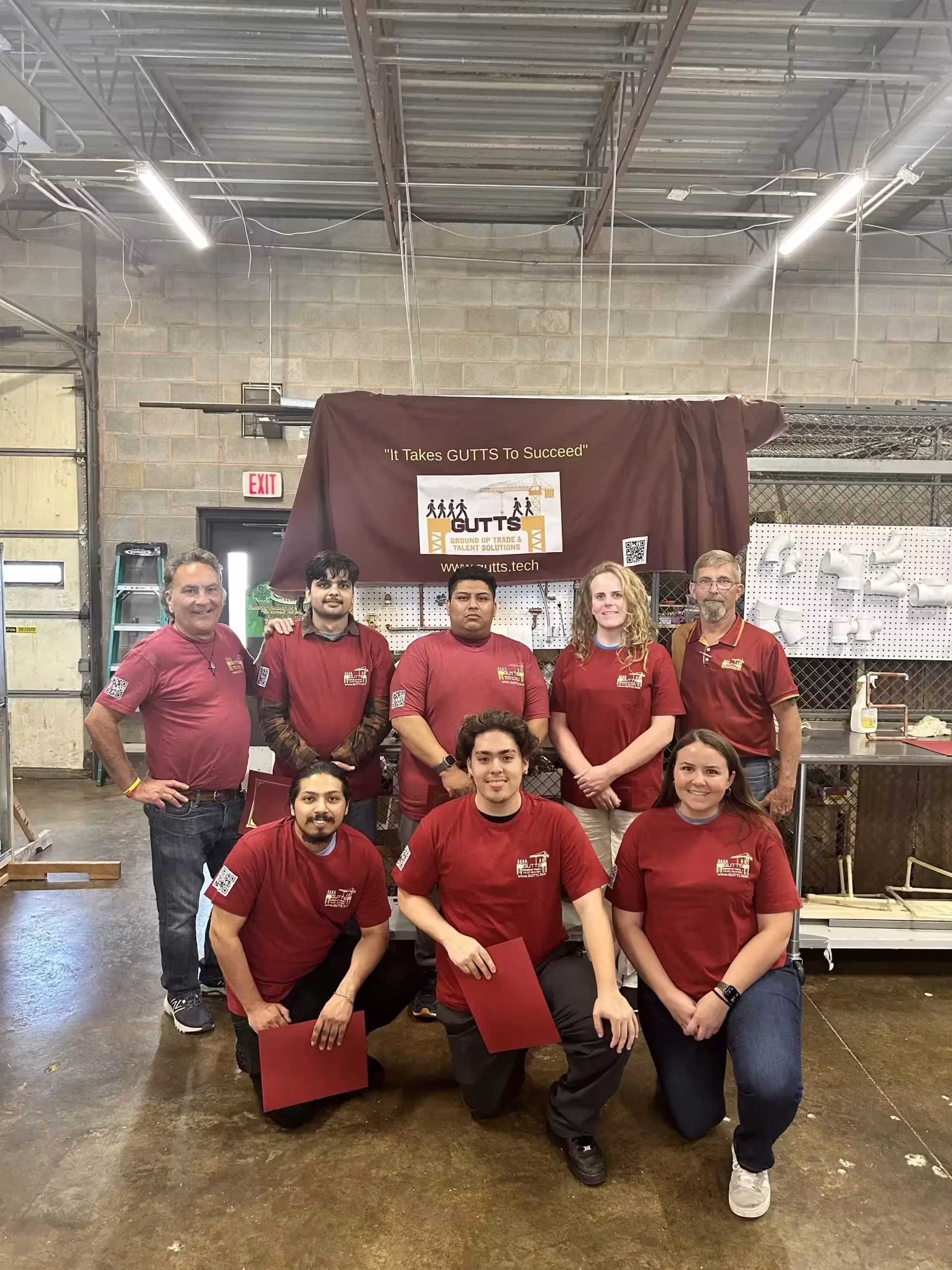 GUTTS team in the workshop with their It Takes GUTTS To Succeed banner